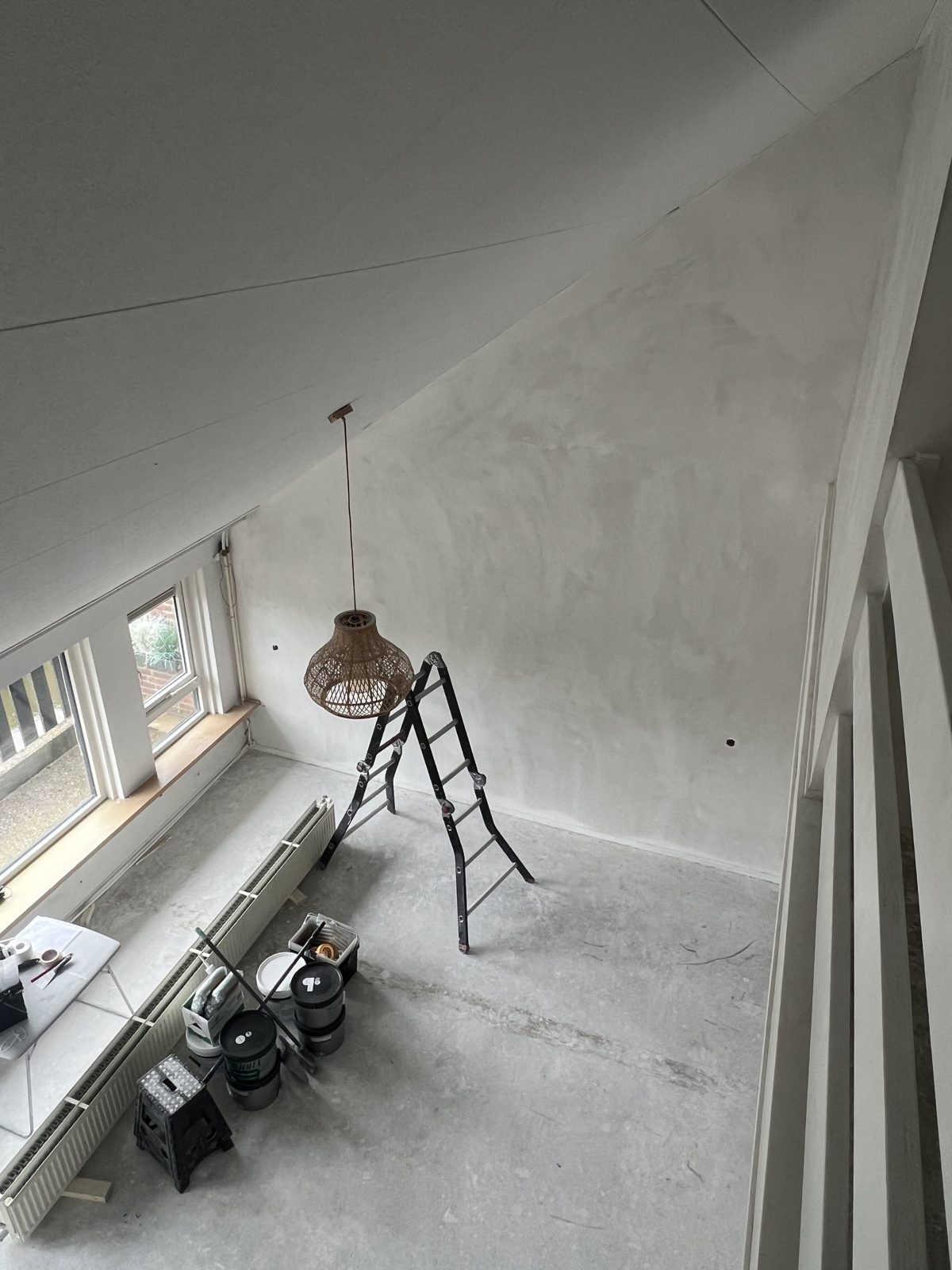 Vers gestuukte zolderkamer met hanglamp, ladder en verfemmers